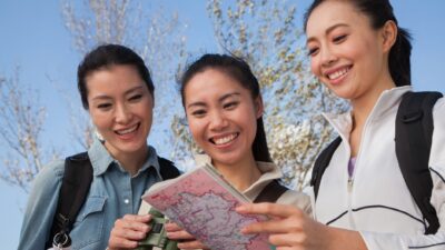 Three young women on holidays smile at they look at a map.