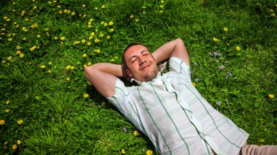 A happy, smiling man stretches out among yellow daisies in the green grass, dreaming of success.