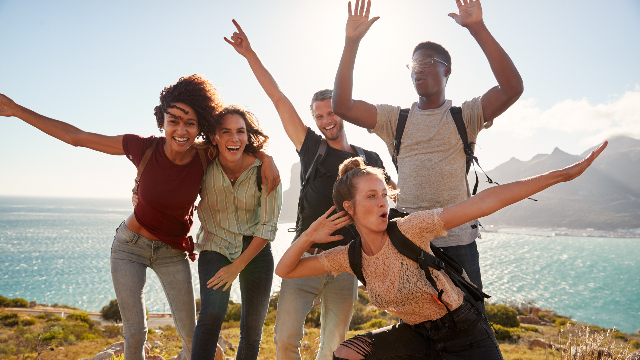 Five happy young friends on the coast, dabbing and raising their arms in the air.