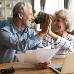 A mature-aged couple high-five each other as they celebrate a financial win and early retirement