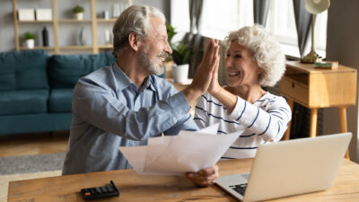 A mature-aged couple high-five each other as they celebrate a financial win and early retirement