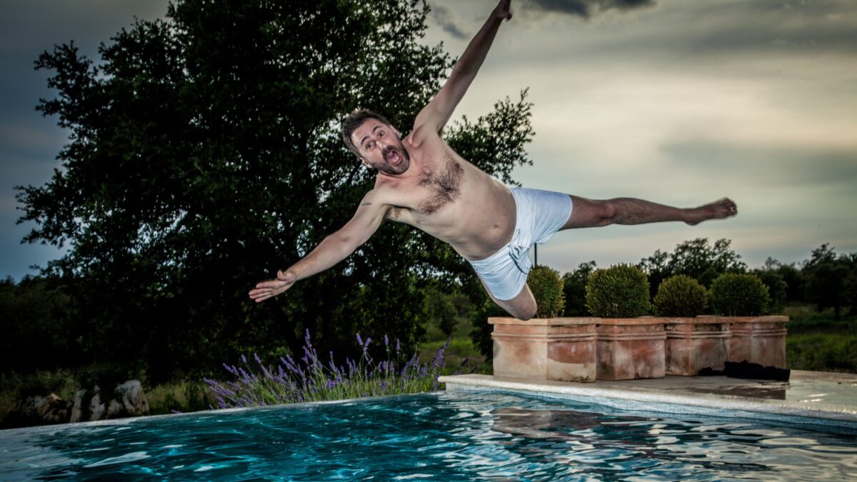 A man with arms spread yells as he plunges into a swimming pool.