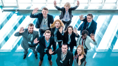 Ten smiling business people wave to the camera after receiving some winning company news.