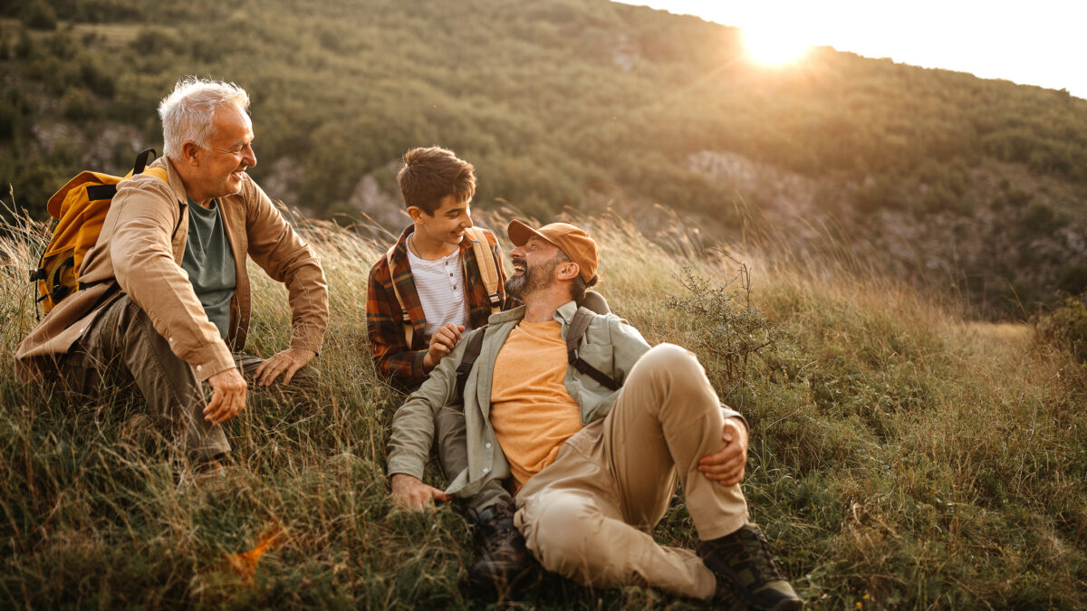 Three generations of male family members enjoy the company as they plan future financial goals together on a trek outdoors.