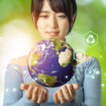 Image of a woman holding a model of earth on a green backdrop.