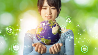 Image of a woman holding a model of earth on a green backdrop.