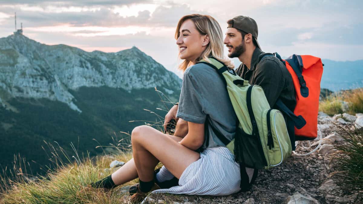 A young smiling couple out hiking enjoy a view from the top of the mountains.