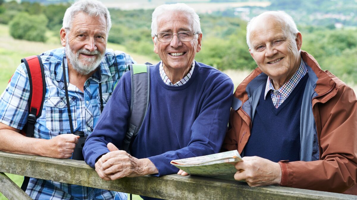 Three fit and healthy mature-aged men smile and check their map while out hiking.