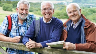 Three fit and healthy mature-aged men smile and check their map while out hiking.