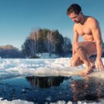 A fit man sits and prepares to dive into a hole made in frozen ice.