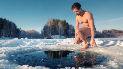 A fit man sits and prepares to dive into a hole made in frozen ice.