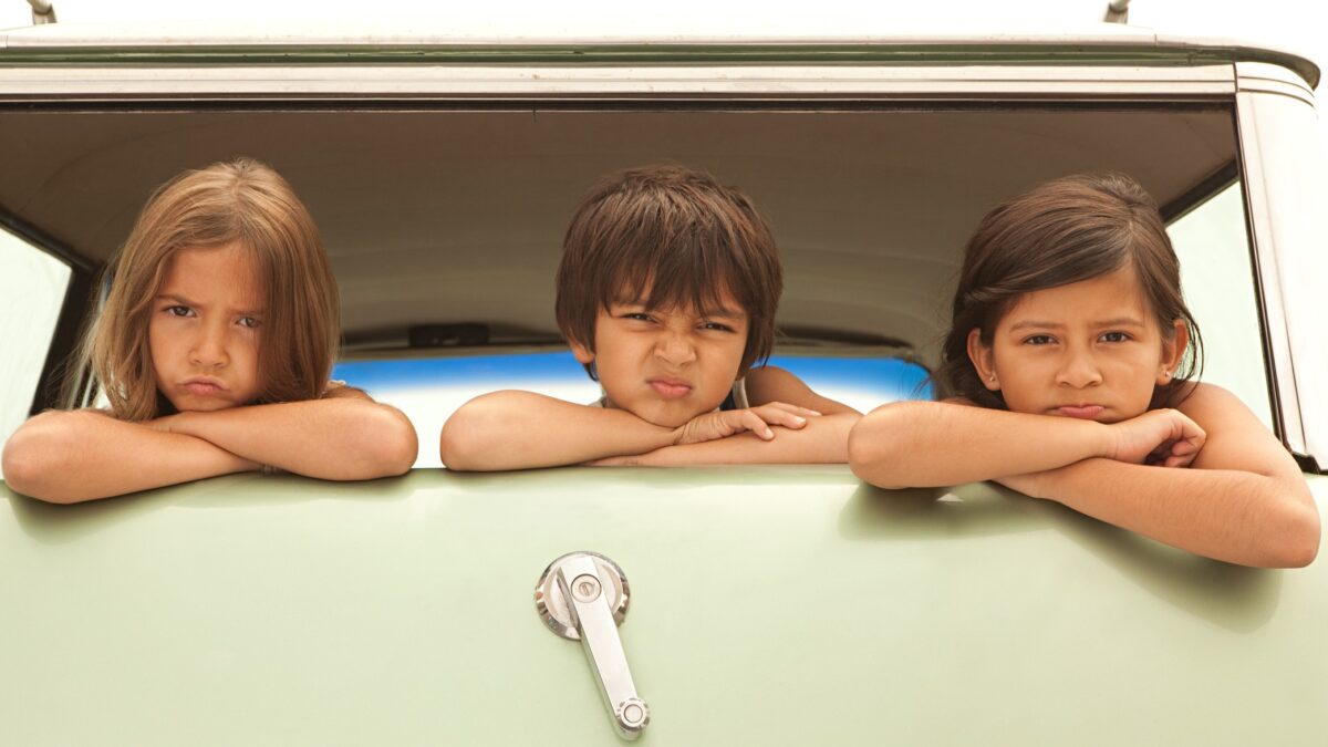 Three cute kids with mixed expressions poke their heads out from the back of a kombi.