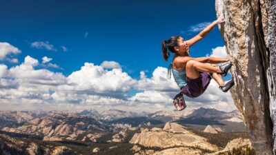 A strong female rock climber holds on to a precarious cliff face by her fingernails.