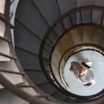 A man stands at the bottom of a spiral staircase looking up.