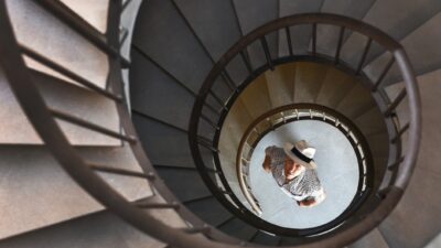 A man stands at the bottom of a spiral staircase looking up.