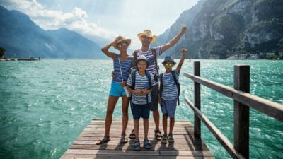 A happy family of four on holidays stand on a jetty and cheer.