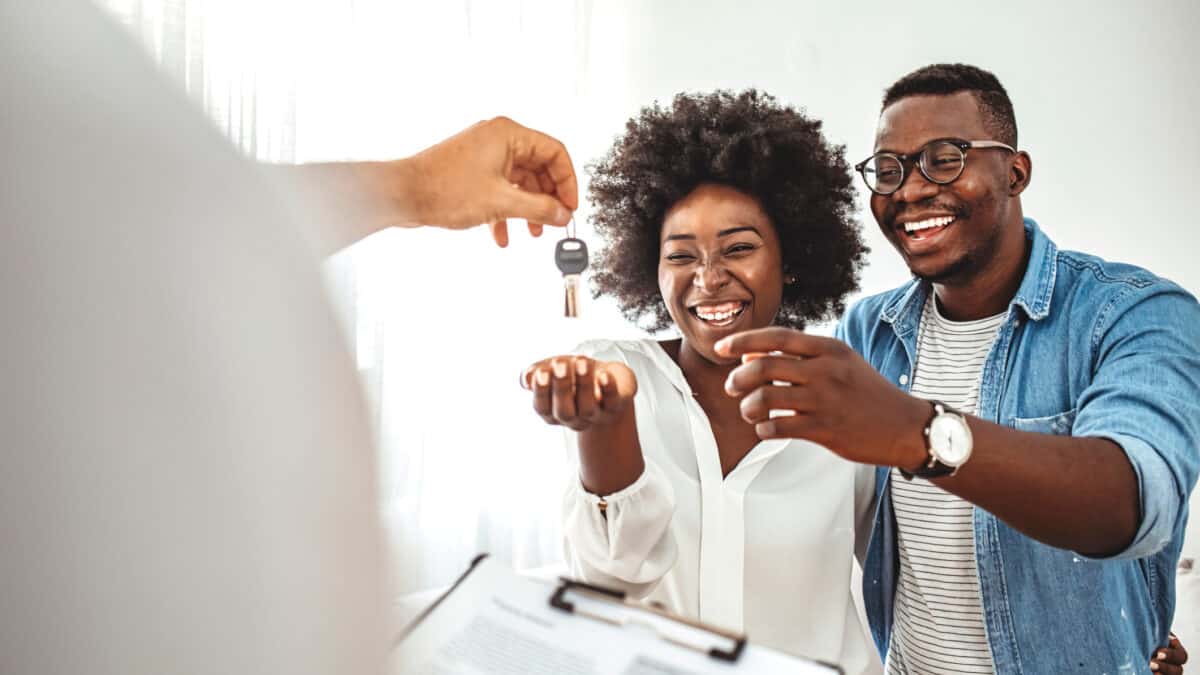 Happy homeowners receiving their new house keys from a real estate agent at office.