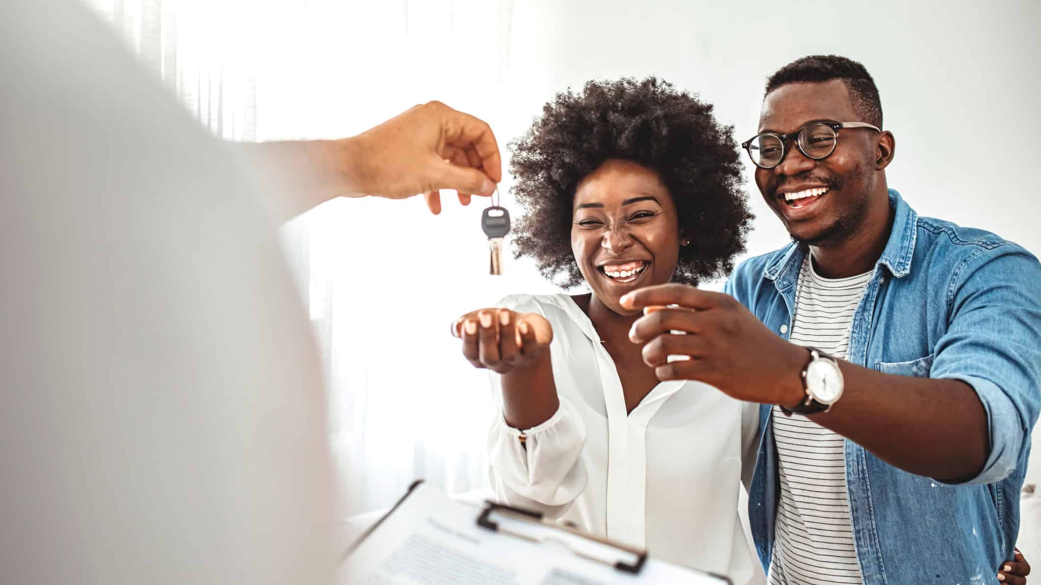 Happy homeowners receiving their new house keys from a real estate agent at office.