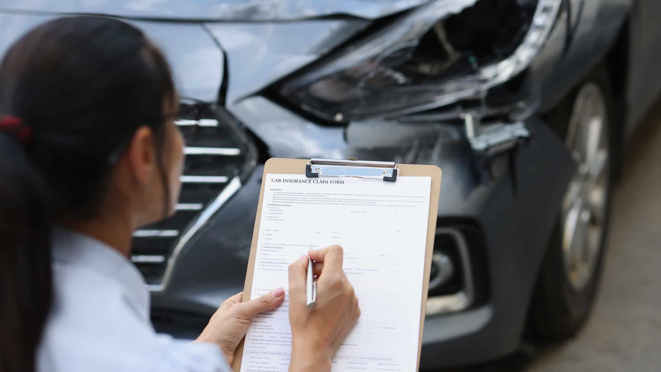 Woman insurance agent fills out insurance form for car damage after traffic accident.