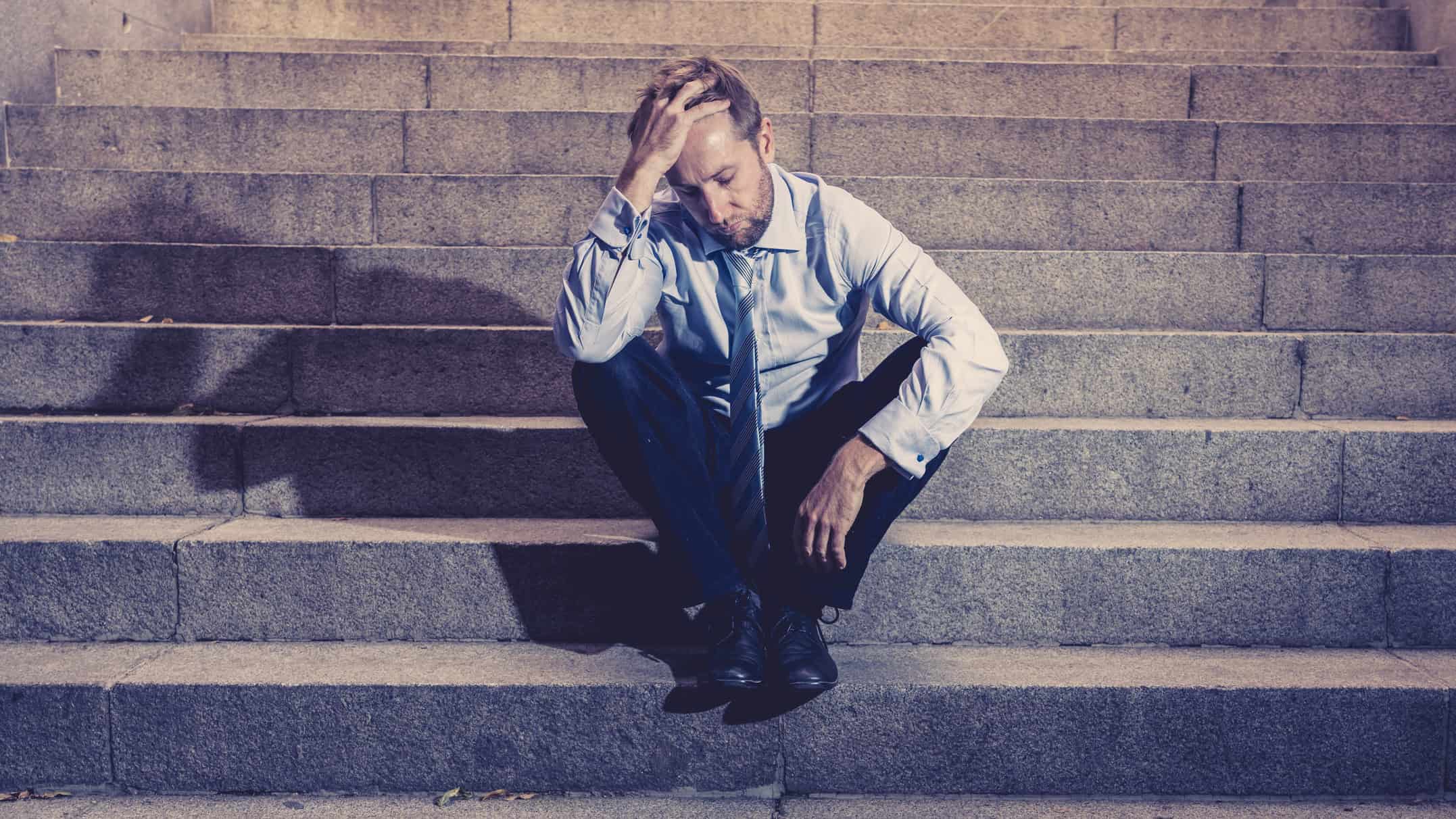 Young businessman lost in depression on stairs.