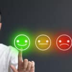 Man pressing smiley face emoji on digital touch screen next a neutral faced and sad faced emoji.