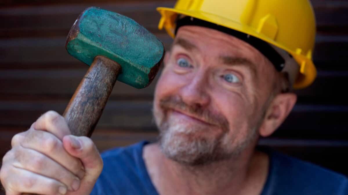 A man holds a green hammer while wearing a yellow hardhat.