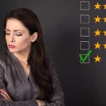 Unhappy business woman in suit with folded arms next to rows of stars with one star box ticked.