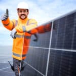 Worker standing by solar panel and holding thumbs up.