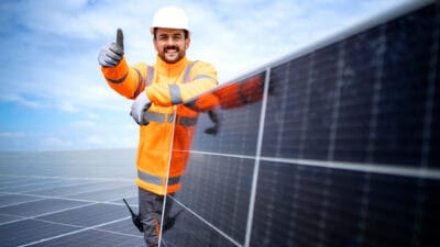 Worker standing by solar panel and holding thumbs up.