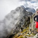 Man smiling on top of rocks with mountains in the background.
