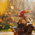 Woman in red hat with scarf rejoicing in the city park with leaves falling.