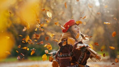 Woman in red hat with scarf rejoicing in the city park with leaves falling.