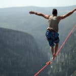 Man trying to balance and walk on a rope attached to a cliff's edge.