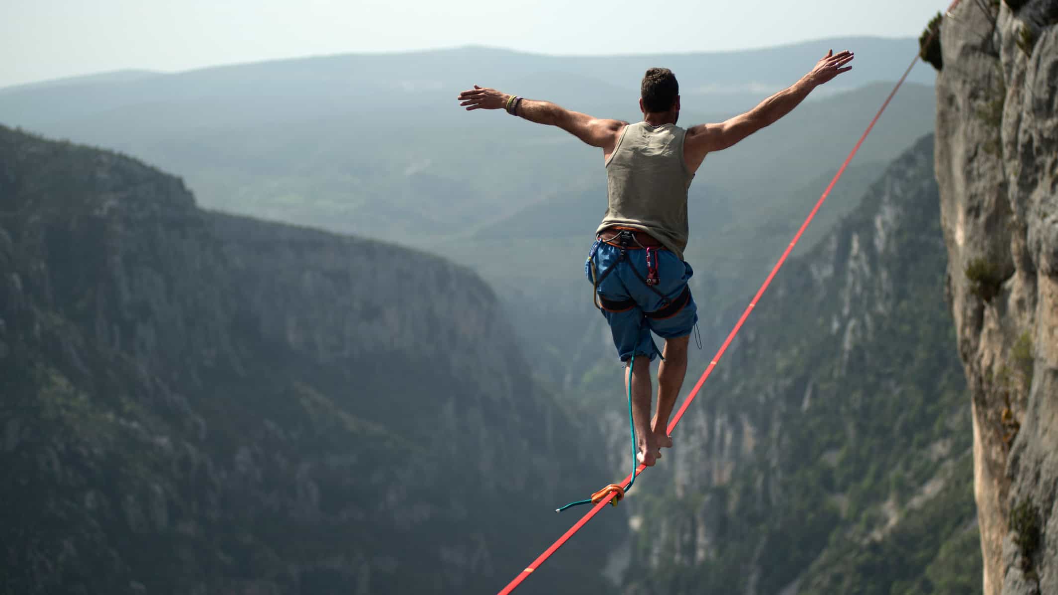 Man trying to balance and walk on a rope attached to a cliff's edge.