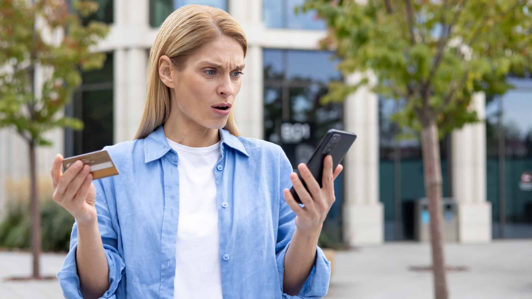 Woman with a concerned look on her face holding a credit card and smartphone.