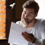 Man with his hand on his face reading a letter with bad news in it