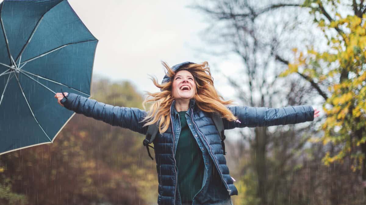 Joyful woman holding out her arms with an umbrella in her hand.