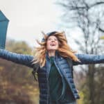 Joyful woman holding out her arms with an umbrella in her hand.