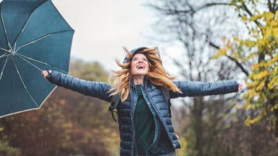 Joyful woman holding out her arms with an umbrella in her hand.