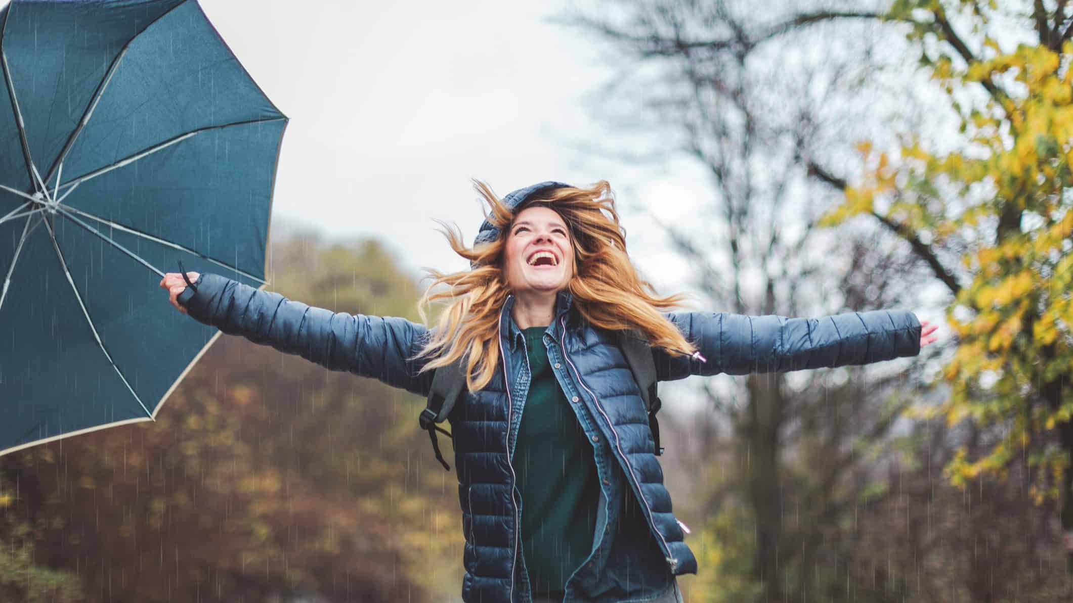 Joyful woman holding out her arms with an umbrella in her hand.