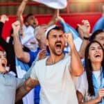 Sport fans cheering at a game in a stadium.