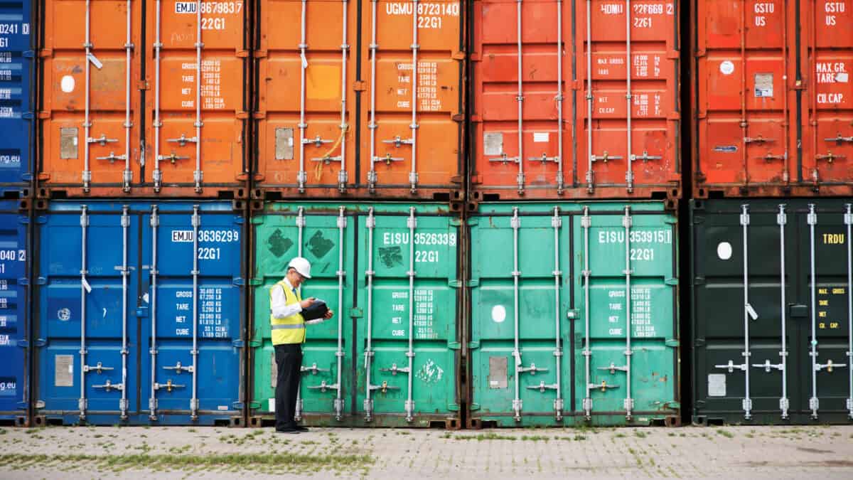 A foreman standing in front of a stack of colourful containers and making notes.