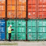 A foreman standing in front of a stack of colourful containers and making notes.