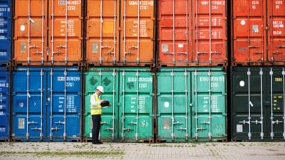 A foreman standing in front of a stack of colourful containers and making notes.