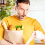 Surprised man looking at store receipt after shopping, symbolising inflation.