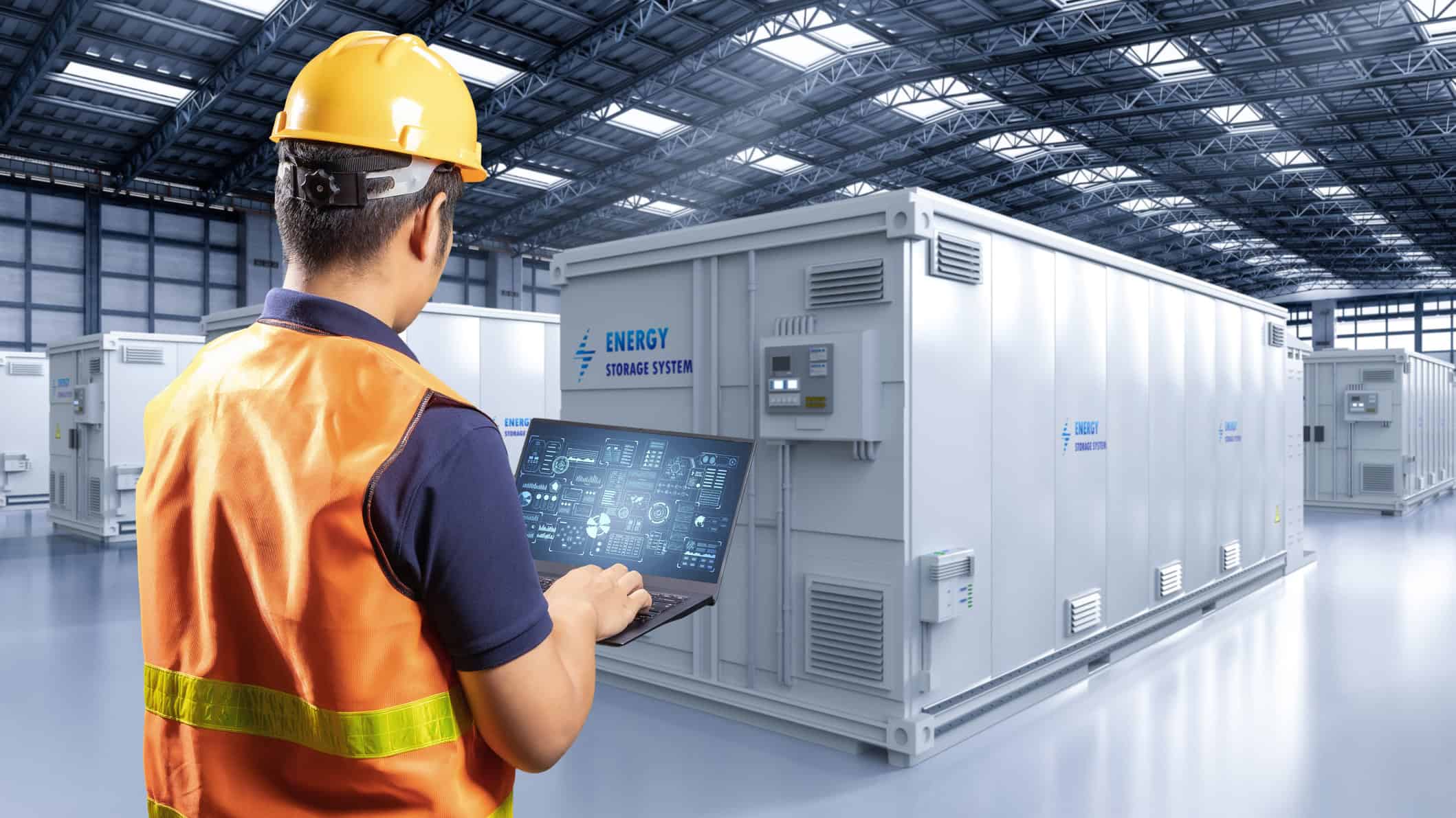 Worker on a laptop in front of an energy storage system in a factory.