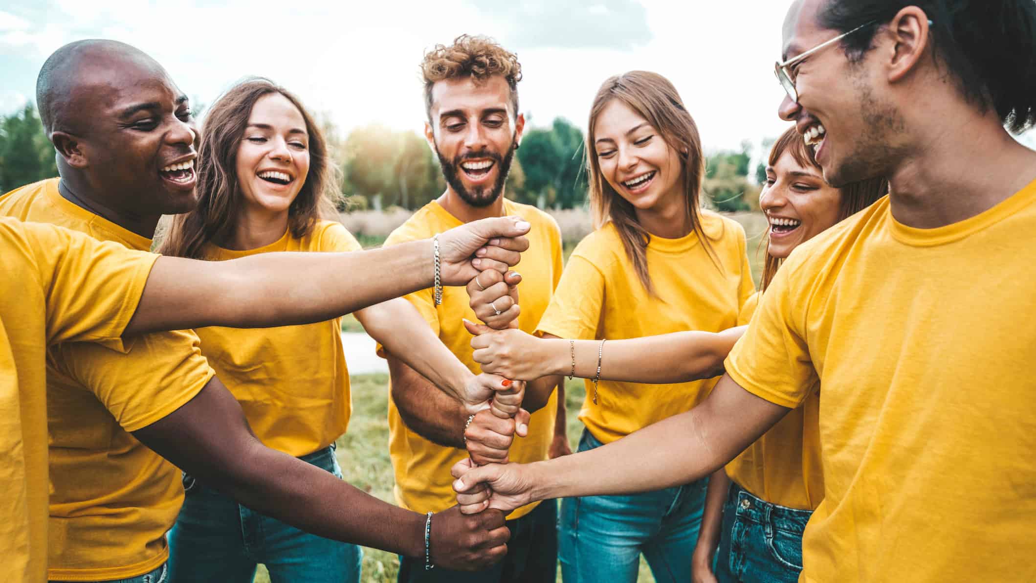 Multiracial happy young people stacking hands outside - University students hugging in college campus - Youth community concept with guys and girls standing together supporting each other.