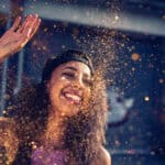 Teen standing in a city street smiling and throwing sparkling gold glitter into the air.