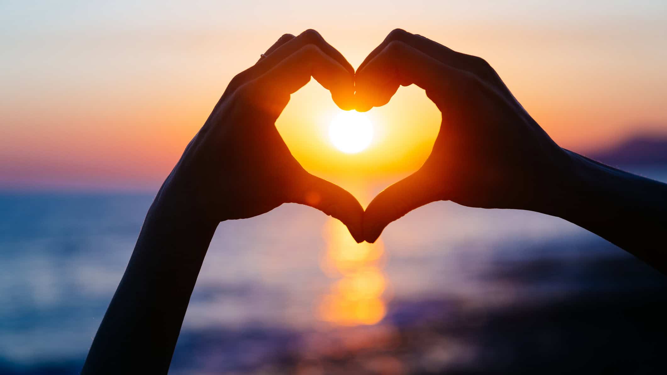 Hands forming a heart shape with sunset silhouette.