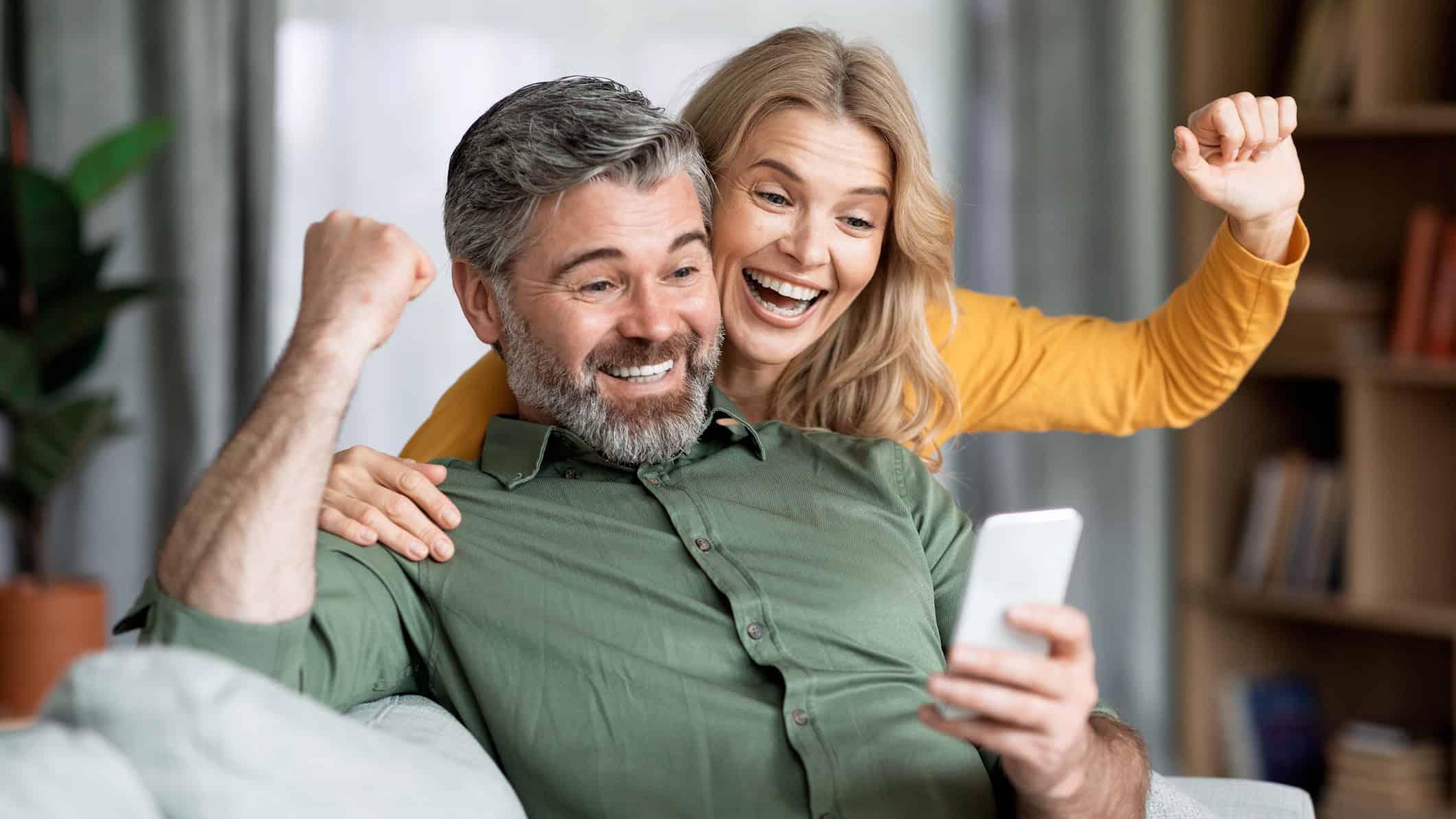 Excited couple celebrating success while looking at smartphone.